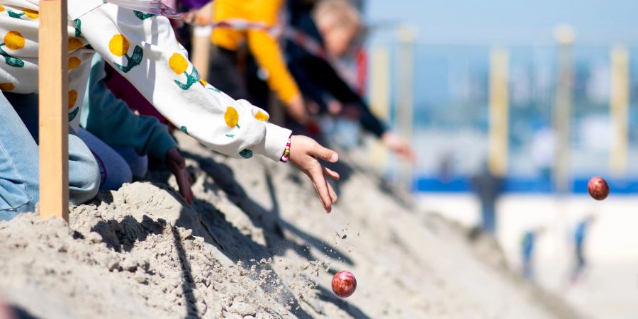 Kinder lassen am Ostersonntag bunte Eier von einer aufgeschütteten Düne am Weststrand von Norderney heruntertrullern.