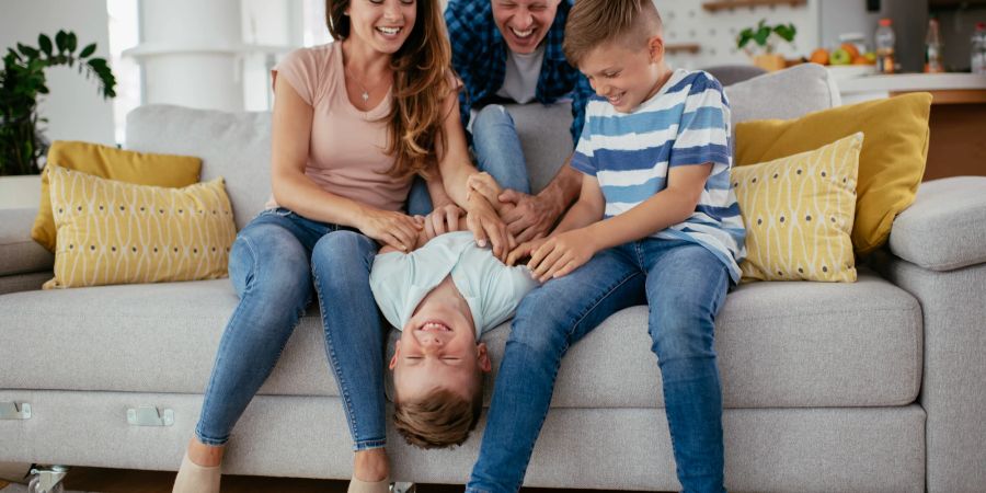 Familie kitzelt kleinen Sohn auf Sofa