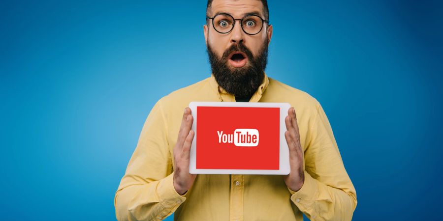 Ein Mann hält ein Tablet hoch mit dem Logo von YouTube und reißt dabei den Mund auf.