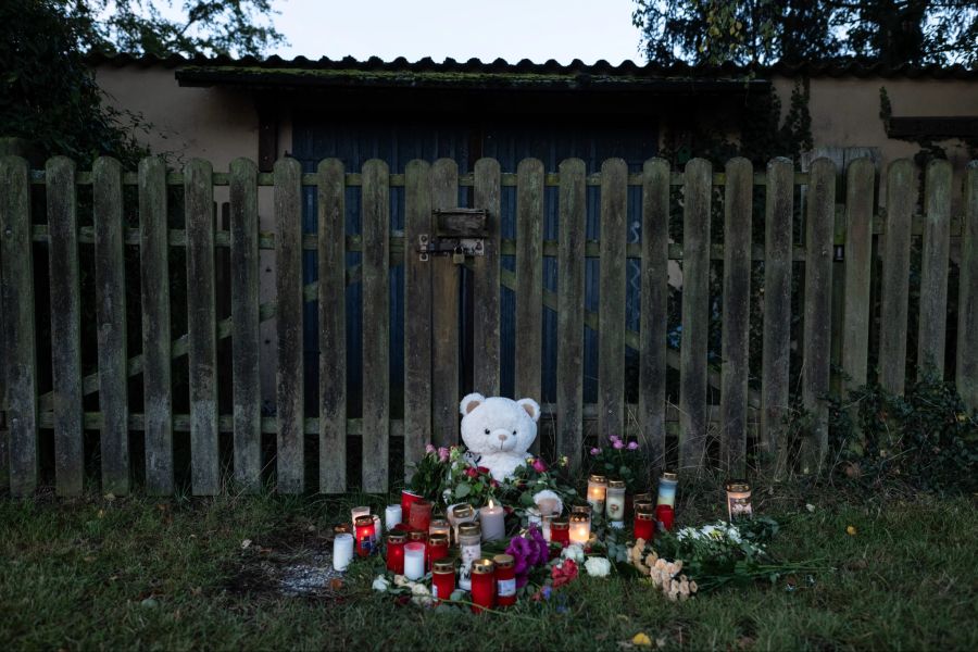 Kerzen, Blumen und ein grosser Plüschteddy sind vor einem Zaun am Fundort zu sehen.