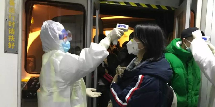 Gesundheitsbeamte kontrollieren in Peking die Körpertemperatur aus Wuhan angereister Passagiere. Foto: Emily Wang/AP/dpa