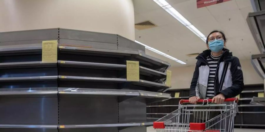 Mit Mundschutz unterwegs: Eine Frau geht in einem Supermarkt in Hongkong einkaufen. Viele Lebensmittelregale sind leer. Foto: Geovien So/SOPA Images via ZUMA Wire/dpa