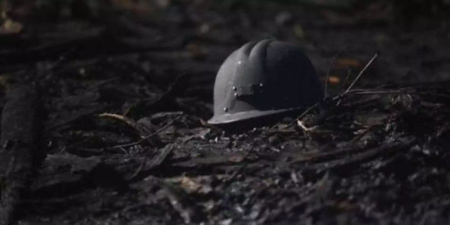 Ein Soldatenhelm liegt auf einem Waldboden voll mit Asche. (Symbolbild)