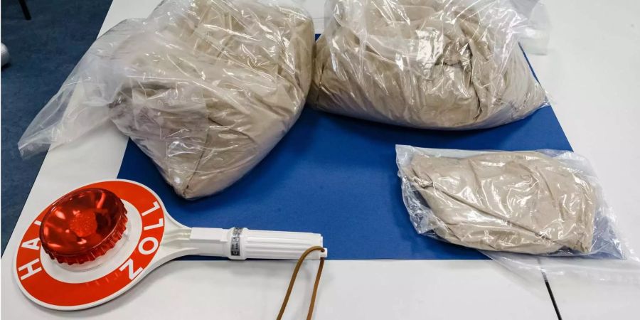 Knapp 12 Kilogramm beschlagnahmtes Heroin im Schwarzmarktwert von ca. 600.000 Euro und eine Signalkelle mit der Aufschrift «Halt Zoll» liegen auf einem Tisch des Zollfahndungsamts Hamburg.