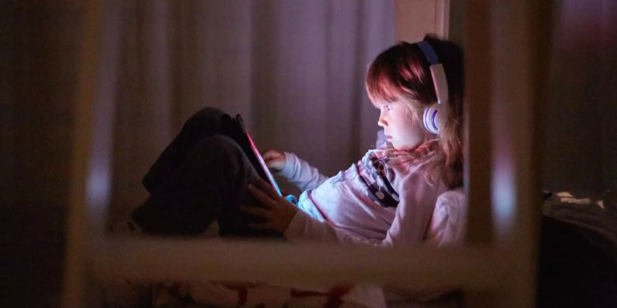 Ein junges Mädchen sitzt auf seinem Bett und benutzt ein Tablet.