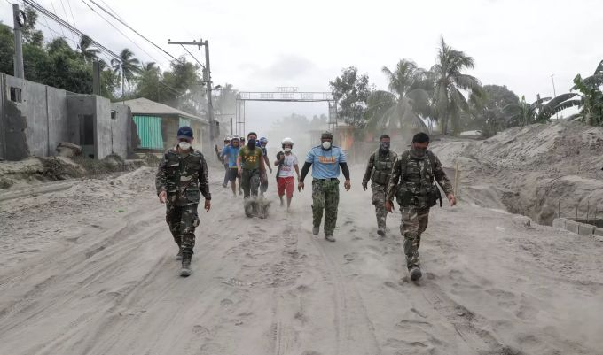Philippinische Polizisten und Soldaten gehen auf einer mit Vulkanasche bedeckten Strasse. taal