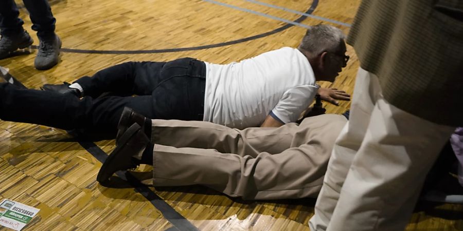 Anhänger des Präsidentschaftskandidaten Villavicencio gehen in Deckung in einer Turnhalle, als Schüsse zu hören sind. Villavicencio war am Mittwoch nach einer Wahlkampfveranstaltung erschossen worden. Foto: Uncredited/API/dpa