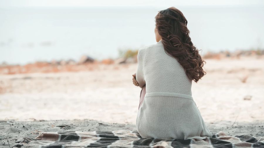 dunkelhaarige frau sitzt am strand, sand