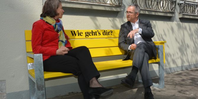 Zwei Personen auf einer gelben Bank.