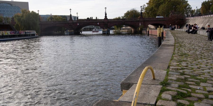 Menschen sitzen unweit der Moltkebrücke an der Spree. In der Nacht zum Freitag war dort ein Hund in die Spree gesprungen, sein Besitzer hinterher. Doch sie kamen zunächst nicht wieder heraus.