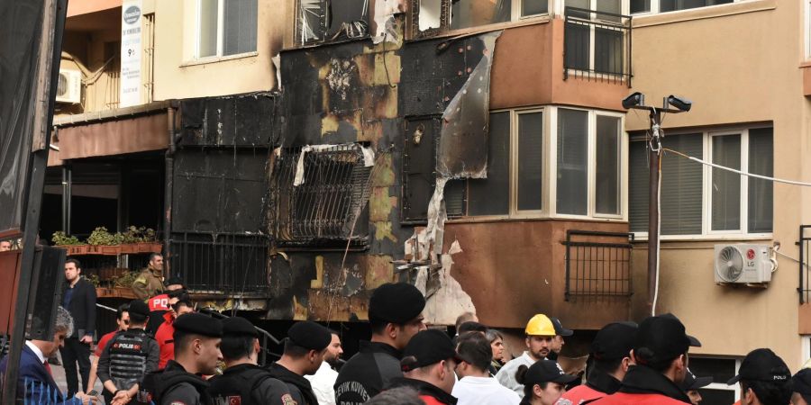 Einsatzkräfte stehen nach einem Brandausbruch vor einem teilweise verbrannten Gebäude.