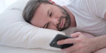 Trauriger Mann im Bett schaut auf Smartphone