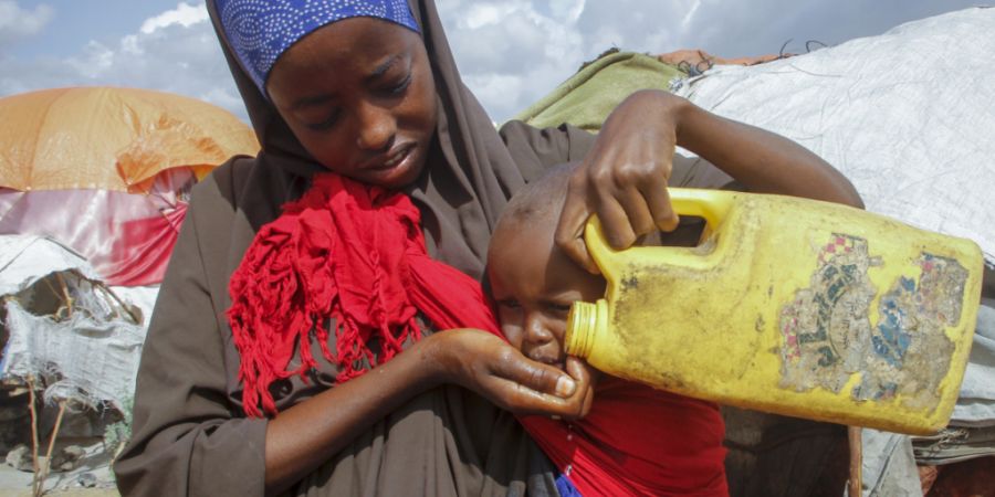 ARCHIV - Eine somalische Frau, die aus den von der Dürre betroffenen Gebieten geflohen ist, gibt ihrem Kind Wasser aus einem Plastikbehälter in einem Lager für Vertriebene am Stadtra...