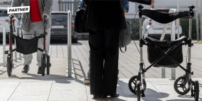Zwei ältere Personen nutzen ihren Rollator auf einem Gehweg.