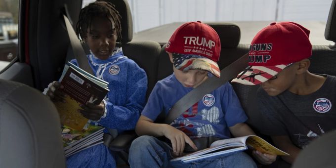 Kinder in den USA mit Trump-Mützen und Trump-Stickern schauen sich auf dem Rücksitz eines Autos Bücher an. (Symbolbild) Donald Trump USA Bücher