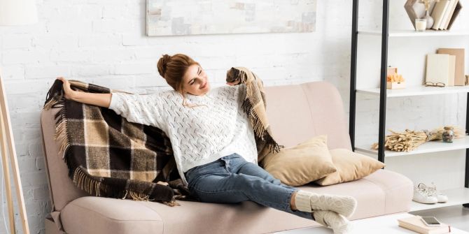 Frau sitzt mit kuscheliger Decke auf Sofa