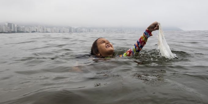 Ein Mädchen holt eine weggeworfene Plastiktüte aus dem Meer in der Nähe des Strandes Copacabana in Rio de Janeiro, Brasilien. Plastiktüte Meer
