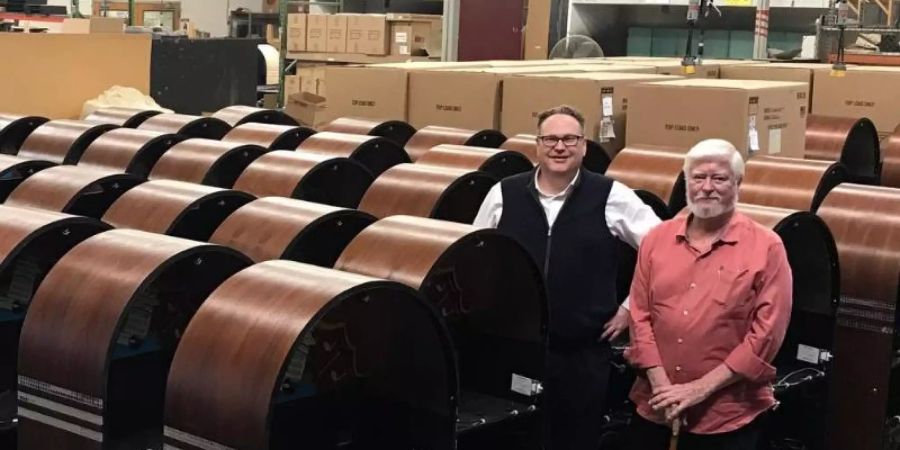 Glenn Streeter (r), Präsident der Firma Rock-Ola, und Besitzer Alexander Walder-Smith stehen in einem Lager voller neuer Jukeboxen. Foto: -/Rock-Ola Manufacturing Corp/dpa
