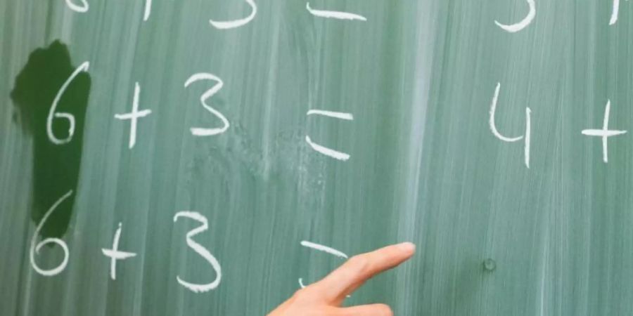 Eine Lehrerin schreibt in einer Schule Rechenaufgaben an eine Tafel. Foto: Julian Stratenschulte/dpa