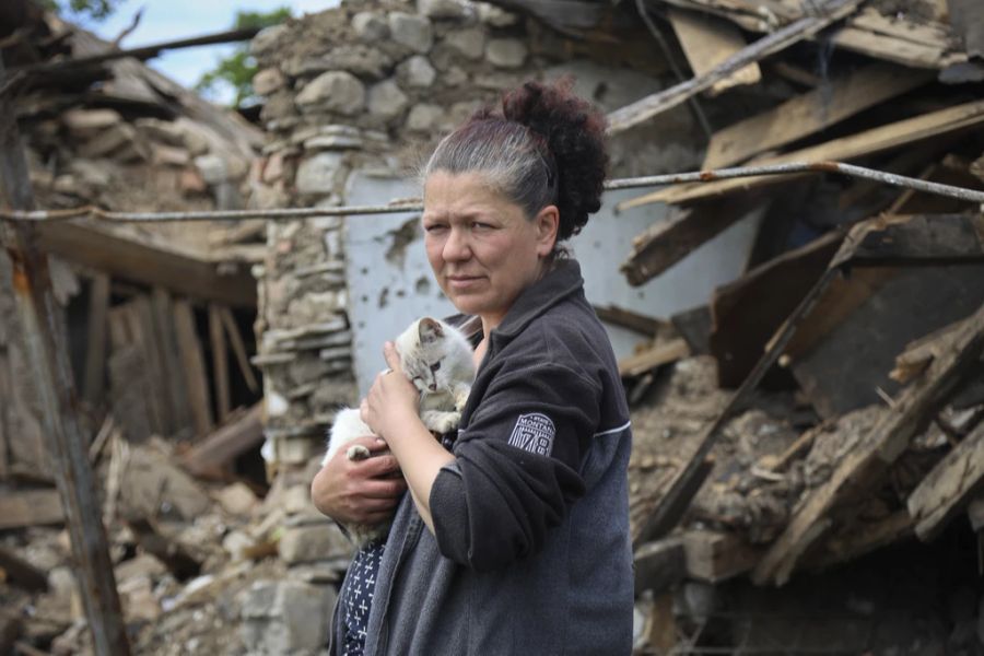 Eine Frau steht mit einer Katze in den Armen vor einem zerstörten Haus in Mariupol.