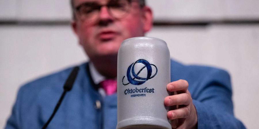 Clemens Baumgärtner (CSU), Referent für Wirtschaft und Arbeit der Landeshauptstadt München und Wiesn-Chef, zeigt das neue Logo des Oktoberfests auf einem Bierkrug.