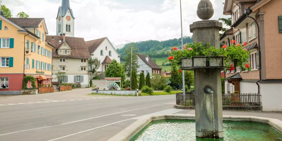 Dorfbrunnen bei der Hauptstrasse in Nesslau. Im Hintergrund steht die reformierte Kirche von Nesslau.