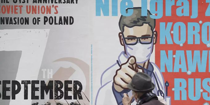Ein Passant geht an einem Plakat (r) vorbei, das vor einer Vernachlässigung der Symptome einer Corona-Infektion warnt. Foto: Czarek Sokolowski/AP/dpa corona