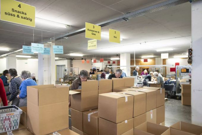 Freiwillige Helfer des SRK sortieren Spenden an Paketen in einem Logistikzentrum. SRK Weihnachten Pakete Spenden