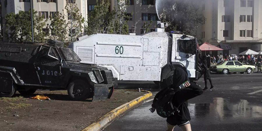 Eine Demonstrantin wirft eine Flasche auf einen Wasserwerfer der Polizei während einer Demonstration in Santiago de Chile am Internationalen Frauentag. Foto: Esteban Felix/AP/dpa