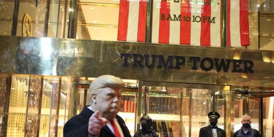 Ein Mann mit einer Trump-Maske in der Hand gestikuliert vor dem Trump Tower, der von einem Polizisten einer Spezialeinheit des NYPD auf der 5th Avenue in Manhattan am Vorabend der Präsidentschaftswahlen gesichert wird. Foto: Marie Le Ble/ZUMA Wire/dpa