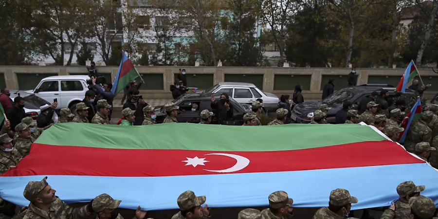 Aserbaidschanische Soldaten tragen eine grosse Fahne in den Farben ihrer Nationalflagge, während sie die Rückgabe der Region Latschin feiern. Foto: Emrah Gurel/AP/dpa
