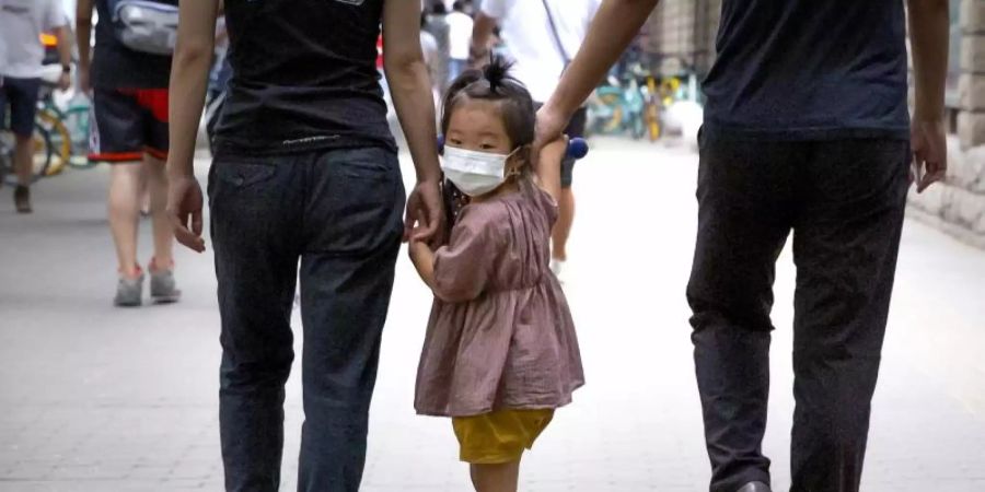 Ein kleines Mädchen wird auf ihrem Roller über einen Gehweg in Peking gezogen. Foto: Mark Schiefelbein/AP/dpa