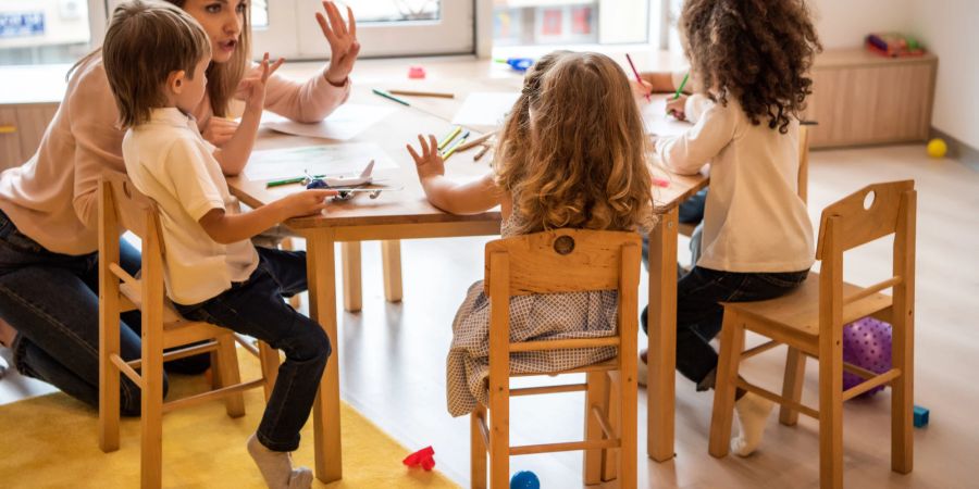 Kinder mit Erzieherin am Tisch