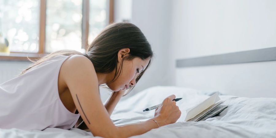 Frau auf Bett mit Stift und Blättern