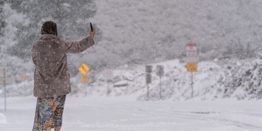 Eine Frau steht auf einer schneebedeckten Strasse und macht ein Selfie im Angeles National Forest.