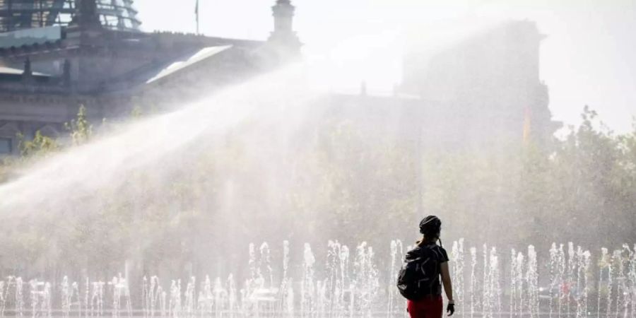 Eine Passantin erfrischt sich in einer Wasserfontäne vor dem Reichstag in Berlin. Nicht nur die Hauptstadt schwitzt. Foto: Kay Nietfeld