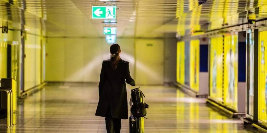 Eine Frau geht mit ihrem Koffer durch einen leeren Gang am Flughafen. Foto: Andreas Arnold/dpa