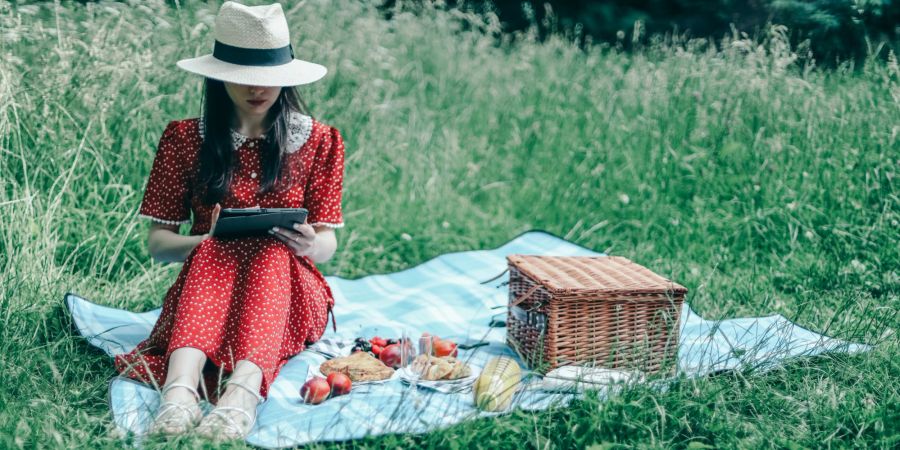 Frau macht Picknick im Freien und liest.