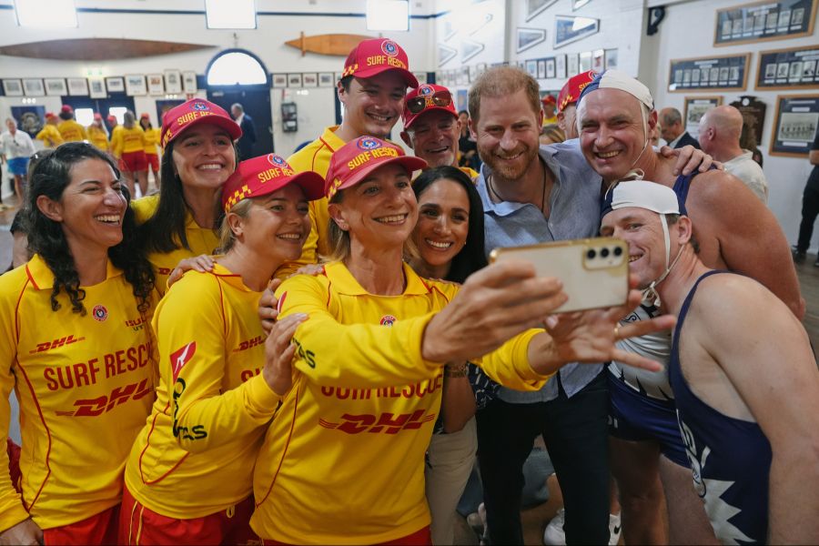Harry und Meghan posieren mit Rettungsschwimmern und Gästen für ein gemeinsames Selfie.