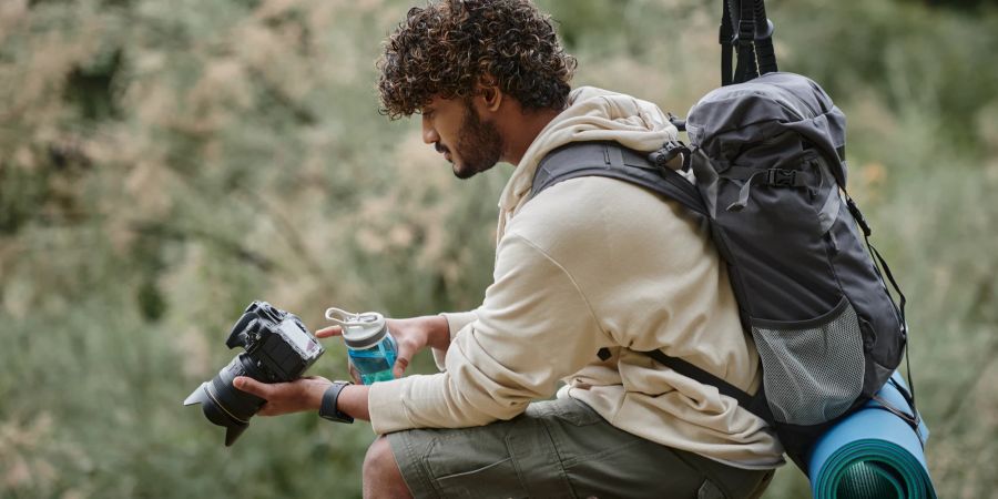 Lockiger Tourist mit professioneller Kamera und Wanderrucksack.