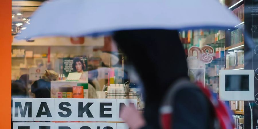 Eine Passantin geht mit einem Regenschirm am Schaufenster einer Apotheke vorbei, in dem auf vorrätige Masken hinweisen wird. Foto: Ole Spata/dpa