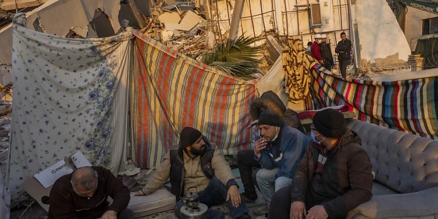 dpatopbilder - Männer sitzen vor den Trümmern bei dem Erdbeben zerstörter Gebäude. Die Zahl der Menschen, die in der Türkei durch das Erdbeben getötet worden sind, ist auf 41 020 gestiegen. Foto: Bernat Armangue/AP/dpa