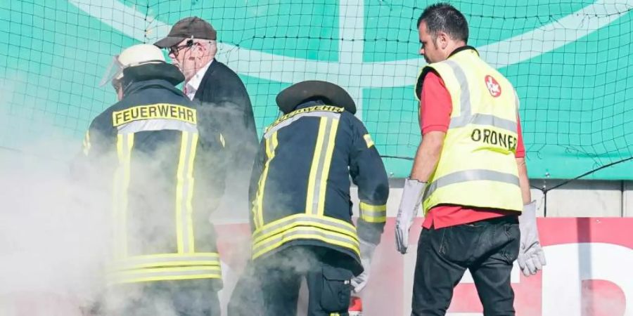 Feuerwehrleute löschen brennende Bengalos, die von Mainzer Fans aufs Spielfeld geworfen wurden. Foto: Uwe Anspach/dpa