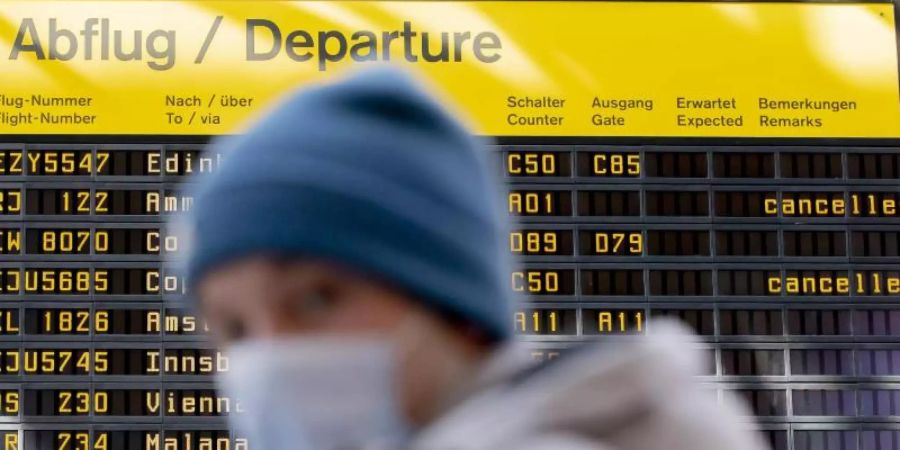 Ein Mann mit Mundschutz steht am Flughafen Berlin-Tegel vor der Anzeigetafel der Abflüge. Foto: Christoph Soeder/dpa