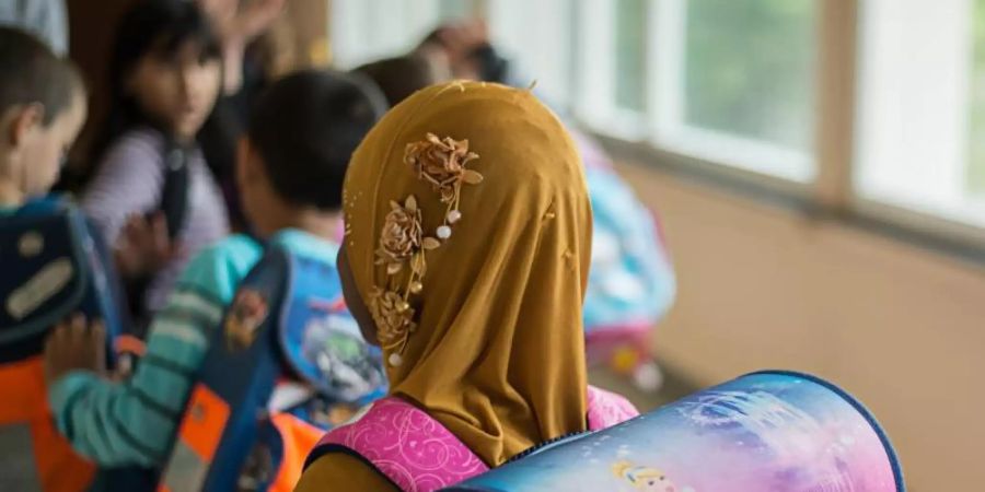 Ein Mädchen mit Kopftuch steht in einer Schule vor einem Klassenzimmer. Foto: Wolfram Kastl/dpa