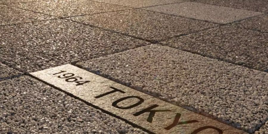 Eine in einen Gehweg eingelassene Tafel mit der Gravur «1964 Tokyo» erinnert an die vergangenen Olympischen Spiele in Japans Hauptstadt. Foto: -/kyodo/dpa