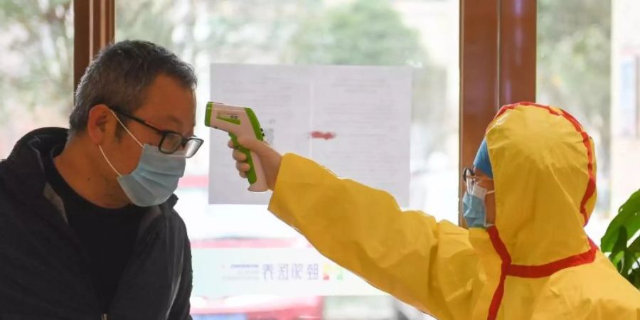 Sorge vor dem Virus: Ein Beamter misst bei einem Kunden eines Friseursalons in China die Temperatur. Foto: Chen Zeguo/XinHua/dpa