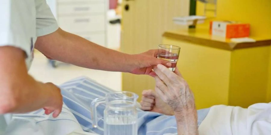 Eine Krankenpflegerin reicht einem Patienten in einem Klinikum ein Glas Wasser. Foto: Daniel Karmann