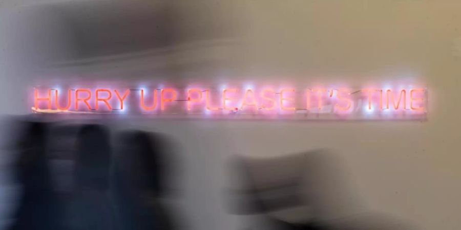 Konferenzteilnehmer gehen bei der UN-Klimakonferenz COP26 in Glasgow an einem Schriftzug der Künstlerin Cornelia Parker vorbei. Zu lesen ist «hurry up please it‘s time» (beeilt euch, es ist Zeit). Foto: Christoph Soeder/dpa