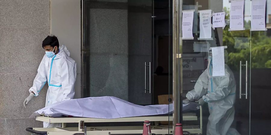 Medizinische Mitarbeiter in Schutzausrüstung transportieren den Leichnam eines Corona-Toten auf einer Trage aus einem Krankenhaus für Corona-Patienten. Foto: Altaf Qadri/AP/dpa